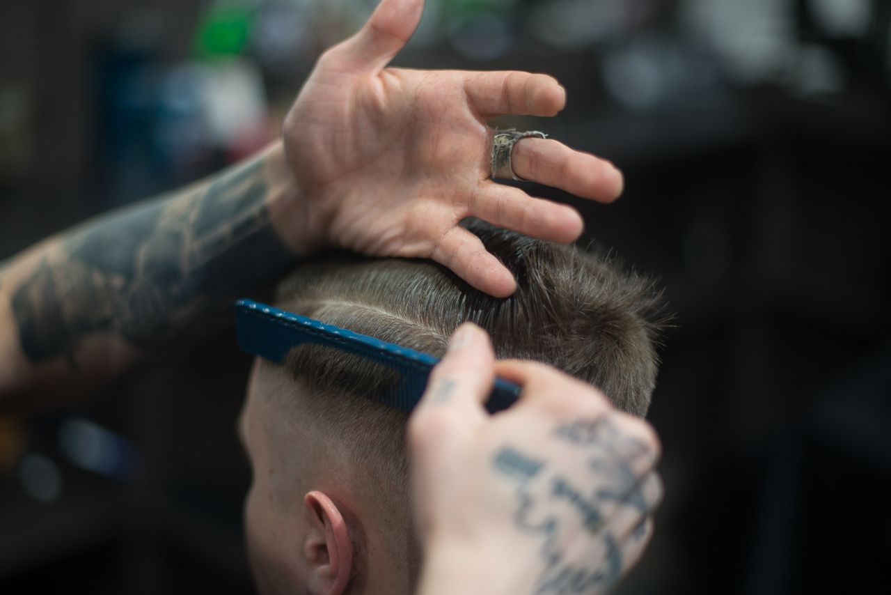 Close-up of precision fade cutting with comb and tattooed barber hands